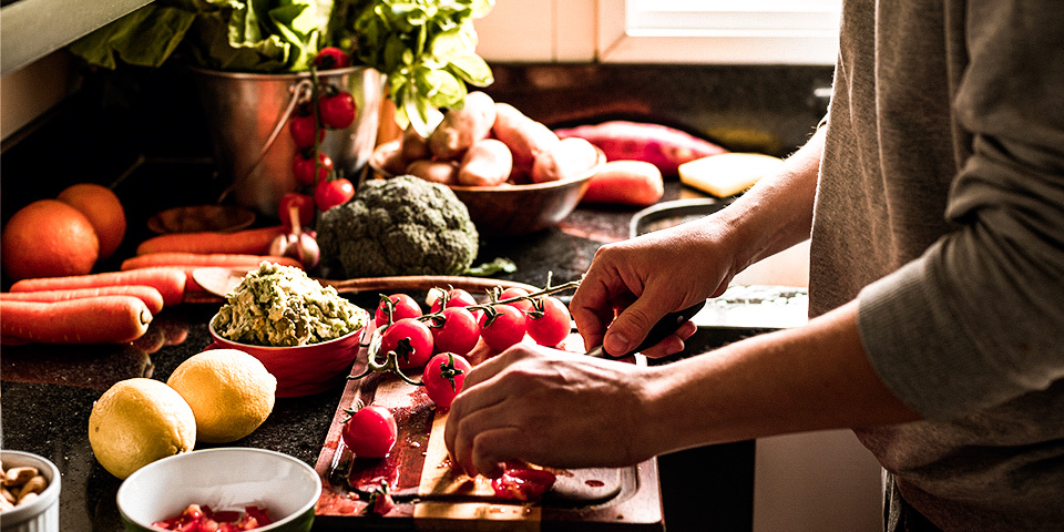 Image of a person prepping a meal in a kitchen filled with fresh vegetables.