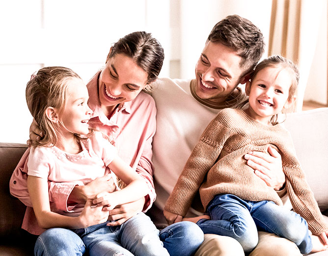 male and female adults sitting on couch with two young children sitting on laps