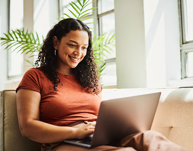 adult female sitting on a couch viewing data on a laptop